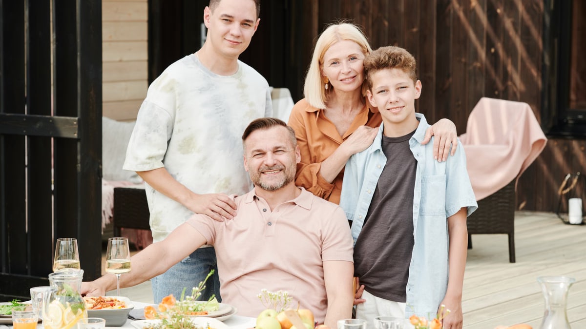 Family of four dining outdoors in a cheerful atmosphere with a table full of food and beverages.