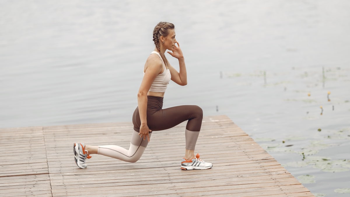 A woman performs lunges on a lakeside wooden deck, showcasing a fit lifestyle outdoors.